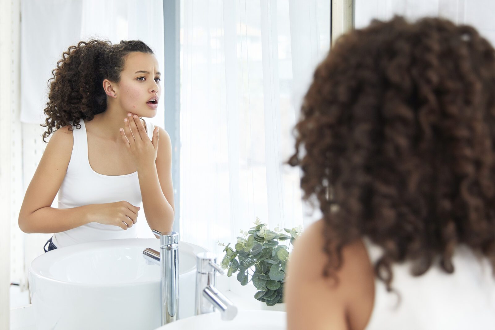 Beautiful young girl touching her face and sees a pimple looking in the mirror in bathroom