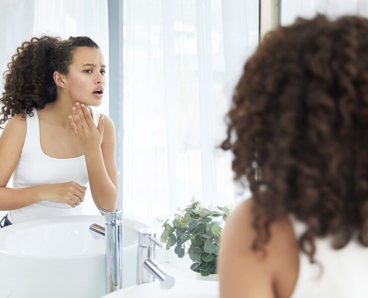 Beautiful young girl touching her face and sees a pimple looking in the mirror in bathroom