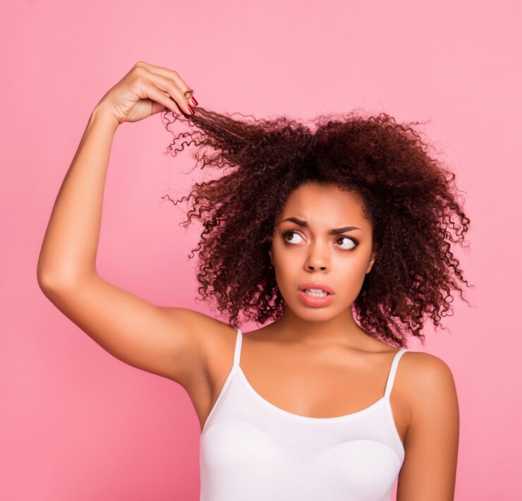 woman holding up a piece of her curly hair and looking at it