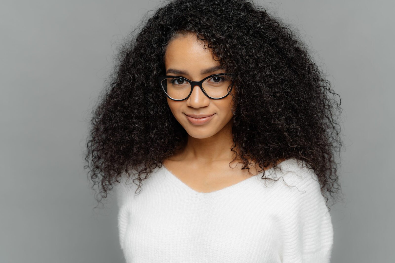 dark skinned female has satisfied expression, bushy curly hair, wears spectacles and white jumper