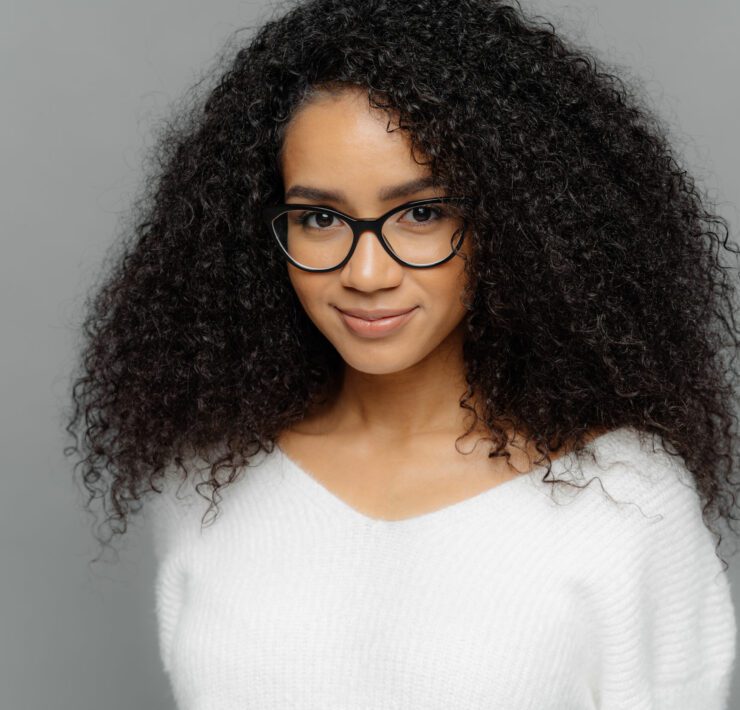 dark skinned female has satisfied expression, bushy curly hair, wears spectacles and white jumper