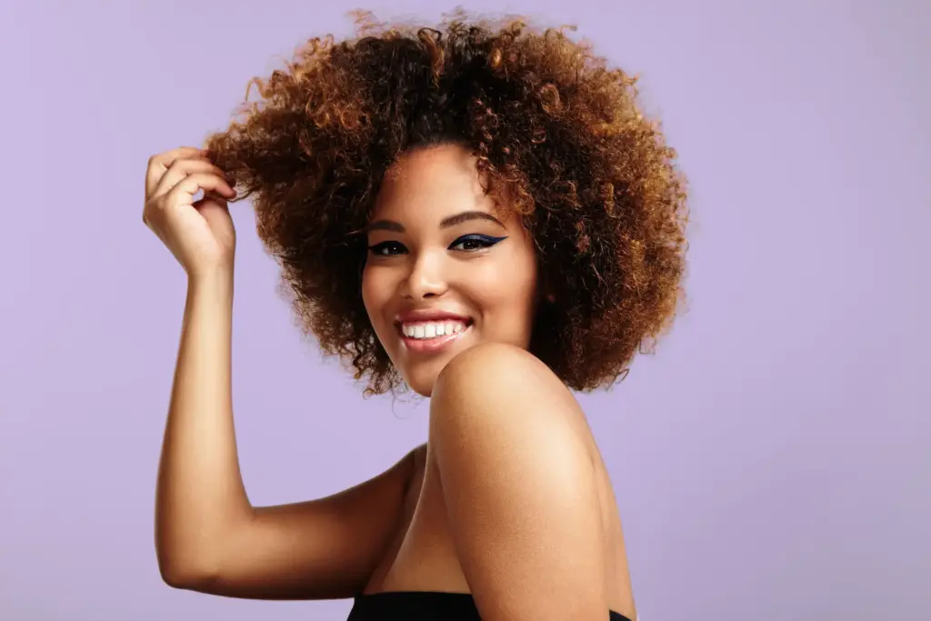 woman with a round afro hair touching a part of it and laughing