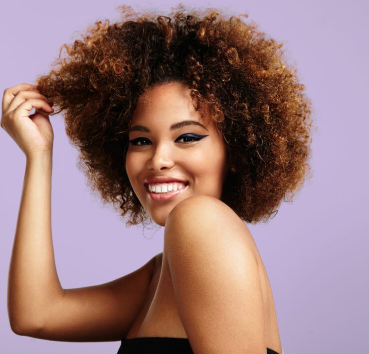woman with a round afro hair touching a part of it and laughing