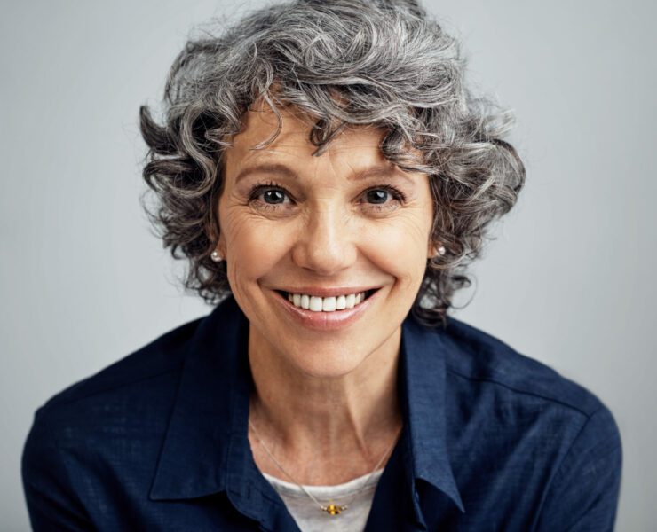 happy mature woman posing against a gray background