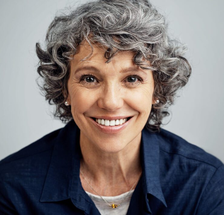 happy mature woman posing against a gray background